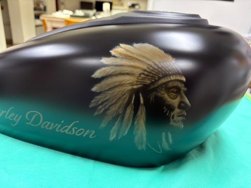 Schwarze Harley-Davidson-Kraftstofftank mit goldener Indianerkopf-Illustration.